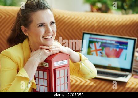 Portrait de la femme élégante heureuse de 40 ans en blouson jaune avec téléphone rouge anglais cabine apprendre l'anglais en ligne sur un ordinateur portable à moderne Banque D'Images
