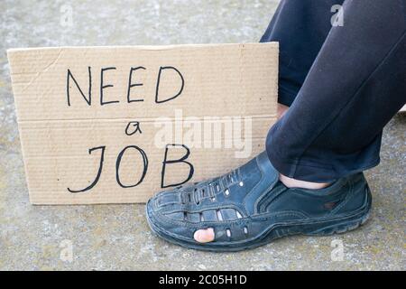 chômage concept homme dans les vieilles chaussures déchirées est assis sur le sol à ses pieds carton signe disant besoin d'un travail Banque D'Images