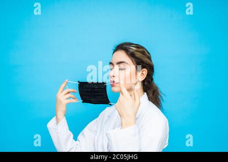 Une jeune femme en costume d'urgicien porte un masque de protection sur son visage et des gants sur les mains se posant sur un fond bleu. Protection. Env Banque D'Images