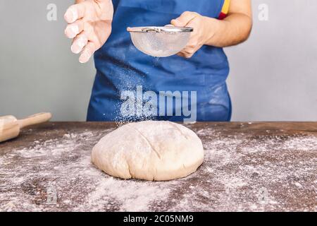 personne méconnaissable mettant de la farine sur une pâte à pain rustique sur une table en bois, concept de nourriture saine à la maison Banque D'Images