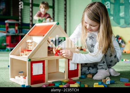 Fille jouant avec une maison de poupée en bois et des personnes de Peg dans une aire de jeux intérieure Banque D'Images