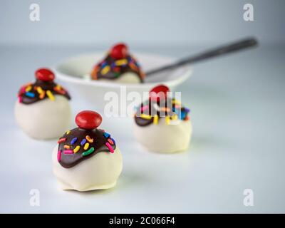 Boules à gâteau en forme de banane avec revêtement blanc, bruine de chocolat couverte de saupoudres et cerise sur le dessus avec un bol blanc et une cuillère. Banque D'Images