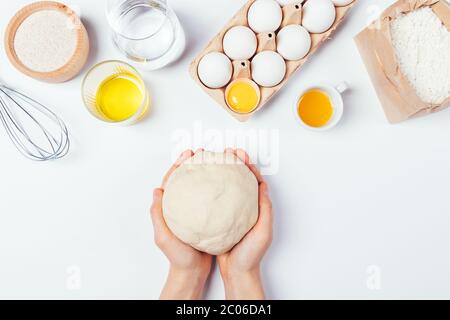 Mains de femme tenant la pâte maison de levure à côté des ingrédients farine de grain entier, huile d'olive, oeufs, eau et miel sur table de cuisine blanche avec copie sp Banque D'Images