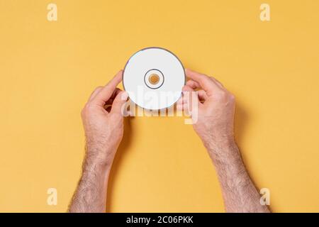 Mains de sexe masculin tenant un CD-DVD devant un fond jaune, modèle de maquette modifiable pour votre conception, chemin de sélection d'étiquette inclus Banque D'Images