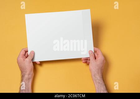 Mains de sexe masculin tenant une enveloppe en papier A4, modèle de maquette modifiable pour votre conception, chemin de sélection inclus Banque D'Images