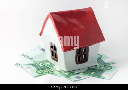 petite maison en porcelaine blanche avec un toit rouge et de l'argent en euros, les billets de banque louent l'achat d'un realtor sur fond blanc isolé Banque D'Images