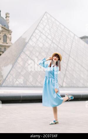 PARIS, FRANCE - 17 septembre 2019 : jeune femme touriste en chapeau de paille et robe bleue marchant près des célèbres pyramides de verre dans le musée du Louvre, le monde Banque D'Images