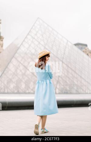 PARIS, FRANCE - 17 septembre 2019 : vue arrière de la charmante jeune femme en robe bleue, debout devant la pyramide de verre au Musée du Louvre Banque D'Images