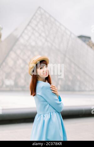 PARIS, FRANCE - 17 septembre 2019 : jolie femme élégante et jeune rouge vêtue de robe bleue, posant à la caméra en face de la pyramide de verre Banque D'Images