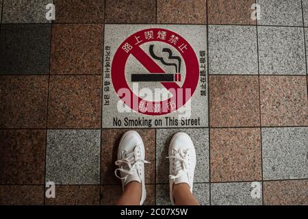 Jambes de baskets debout au-dessus d'un panneau interdiction de fumer écrit en japonais à Tokyo Japon Banque D'Images