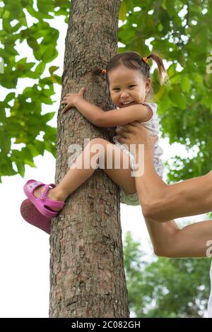 Une petite fille qui s'accroche sur un arbre et qui s'amuse au parc. Enfance drôle. Banque D'Images