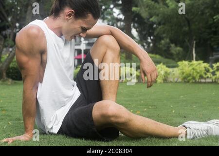 Homme assis sur l'herbe au parc prenant une pause après un entraînement cardio-vasculaire. Banque D'Images