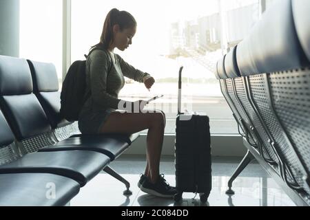 Une personne qui vérifie l'heure sur sa montre en étant assise à la porte d'entrée de l'aéroport en attendant son vol. Banque D'Images