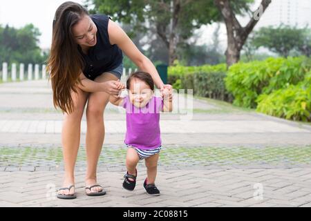 La mère tient le bras de l'enfant tout en lui enseignant de marcher Banque D'Images
