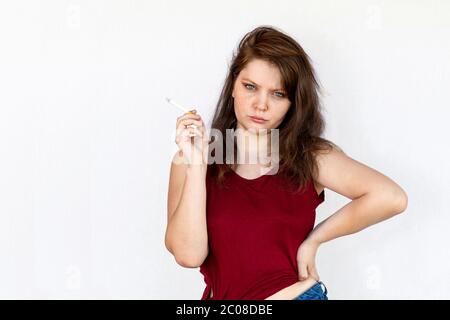 Brunette fille avec cigarette dans la main. Vêtements décontractés, t-shirt rouge et short en denim. Portrait en demi-longueur sur fond blanc. Banque D'Images