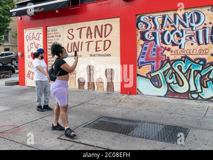 New York, États-Unis. 11 juin 2020. Une femme prend des photos d'artistes locaux du graffiti peints sur des murs de vitrines à bord pour un message visant à guérir les divisions raciales dans la communauté sur la rue Dyckman à New York le 11 juin 2020. Les artistes ont reçu des autorisations des propriétaires d'entreprise pour transformer leurs vitrines récemment intégrées en toiles géantes. Les récentes manifestations ont été déclenchées par la mort de George Floyd aux mains de la police de Minneapolis. (Photo de Lev Radin/Sipa USA) crédit: SIPA USA/Alay Live News Banque D'Images