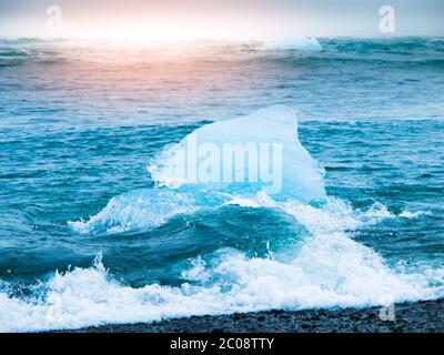 Les icebergs ont été écrasés par les vagues de la mer sur la plage noire au lever du soleil près du lac glacier de Jokulsarlon, en Islande. Banque D'Images