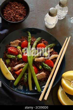 Concept d'alimentation saine. Salade fraîche avec riz rouge, thon, asperges, tomates et citron sur fond sombre. Vue de dessus. Banque D'Images