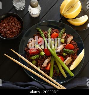 Concept d'alimentation saine. Salade fraîche avec riz rouge, thon, asperges, tomates et citron sur fond sombre. Vue de dessus. Banque D'Images