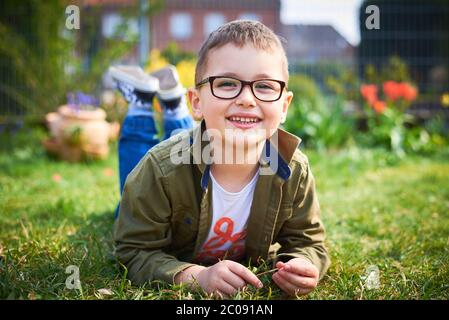 Garçon avec des lunettes assis sur l'herbe et sourire Banque D'Images