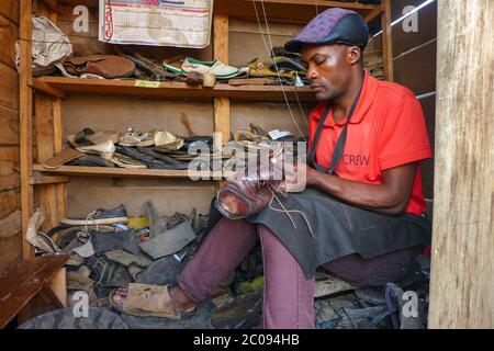 Stino Muhindo attache un vieux pneu au fond d'une chaussure pour créer une nouvelle semelle à Kirumba, République démocratique du Congo. Muhindo rassemble les vieux pneus de voiture des propriétaires de garage locaux et les utilise pour réparer les chaussures dans son magasin, situé dans le quartier de Buhimba. (Merveille Kavira Lungehe, GPJ République démocratique du Congo) Banque D'Images