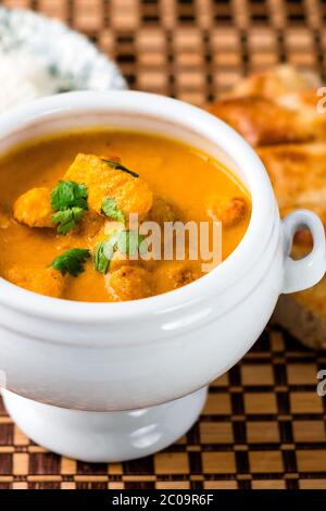 Délicieux plat indien de poulet au beurre servi dans un bol blanc avec du pain naan et du riz sur le côté. Le plat est placé sur un tapis de sol en bois. Banque D'Images