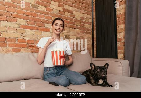 bonne femme tenant le seau à pop-corn et assise avec un joli boudogue français sur le canapé Banque D'Images