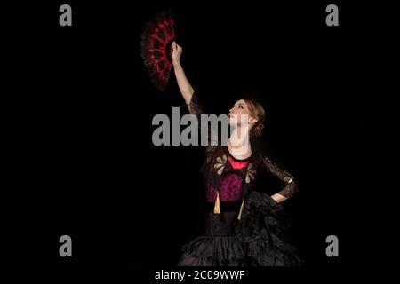magnifique danseur regardant le fan tout en dansant le flamenco isolé sur le noir Banque D'Images