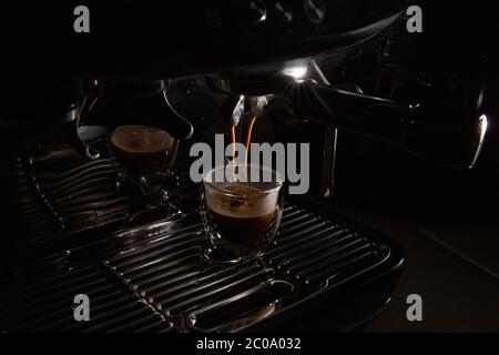 Des gouttes de café sombre s'écoulant dans une tasse à espresso en verre transparent sur une machine à espresso manuelle avec espace pour copier, gros plan Banque D'Images