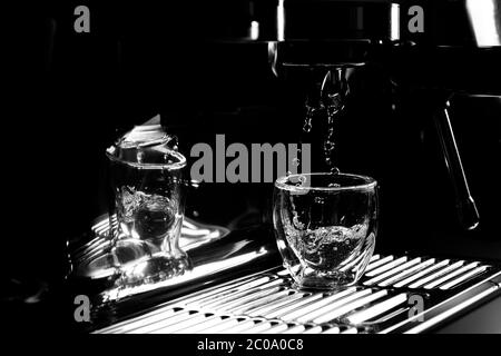 Gros plan de gouttes d'eau chaude qui s'écoulant dans une tasse à espresso transparente provenant d'une machine à café manuelle pour le préchauffage, monochrome, avec espace de copie Banque D'Images