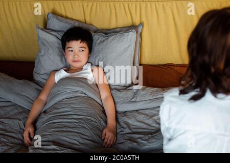 mignon garçon asiatique allongé dans le lit avec mère près de la quarantaine Banque D'Images