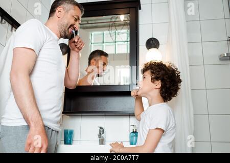 beau père et fils mausseux se brossant les dents dans la salle de bains Banque D'Images