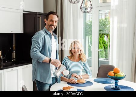 Couple d'âge mûr souriant à l'appareil photo pendant le petit déjeuner dans la cuisine Banque D'Images