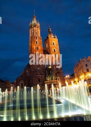 Eglise Sainte Marie avec deux tours différentes la nuit (Cracovie, Pologne). Vue depuis la fontaine. Banque D'Images