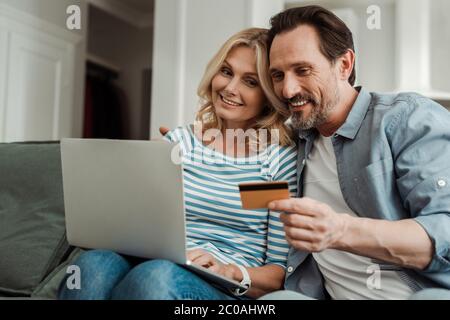 Foyer sélectif de sourire couple mature utilisant la carte de crédit et ordinateur portable sur le canapé Banque D'Images