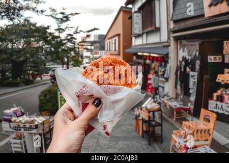 Main femelle tenant un craqueur de maïs épicé traditionnel japonais de la cuisine de rue à Kanazawa au Japon Banque D'Images