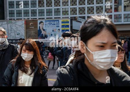 Les personnes portant des masques chirurgicaux à la populaire Shibuya croiser. Publicités et bâtiments en arrière-plan. Banque D'Images