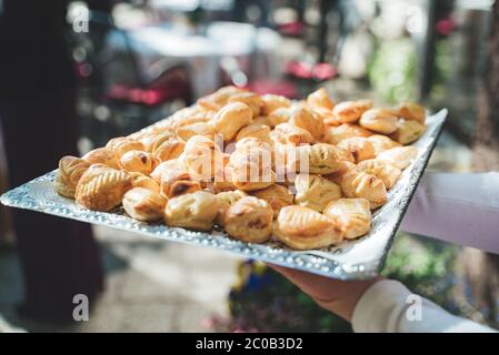 Homme tenant le plateau avec la pâtisserie. Pâtisseries fraîches croustillantes cuites au four, fourrées de fromage ou d'épinards. Concept de célébration, fête, anniversaire ou mariage. Banque D'Images