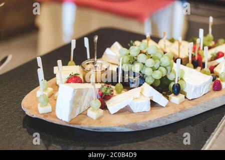 Planche en bois avec tranches de différents types de fromage mûri servi avec des olives, des raisins, des fraises et des framboises. Fête, fête Banque D'Images