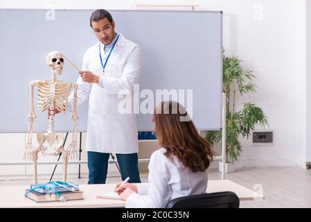Jeune professeur de sexe masculin, squelette et étudiant de sexe féminin dans la salle de classe Banque D'Images