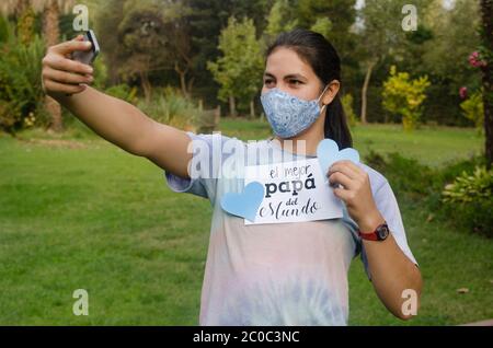 Jeune fille souriant au téléphone portable pendant un appel vidéo à un père à la maison pour la fête des pères. Elle tient une carte blanche avec le texte Happy Pather's Day Banque D'Images