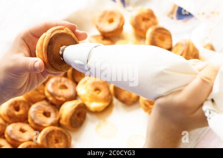 remplir la pâte de profiterolle de crème à l'aide du sachet de pâtisserie de préparation faite maison Banque D'Images