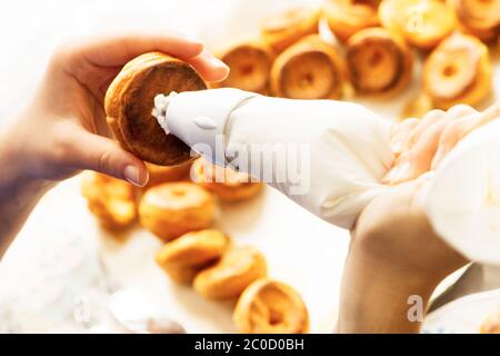 remplir la pâte de profiterolle de crème à l'aide du sachet de pâtisserie de préparation faite maison Banque D'Images