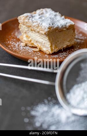 Cremșnit assis sur une plaque. Est fait de pâte filo d'habituellement trois couches avec de la crème sur le dessus et crumble arrosé dessus. Banque D'Images