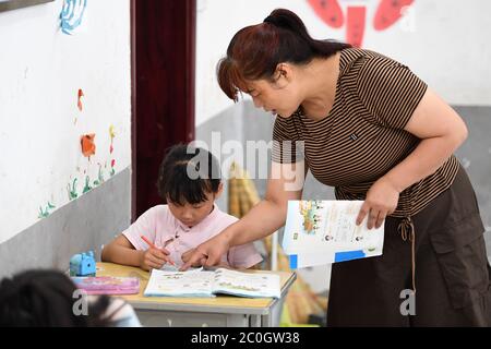 (200612) -- HEFEI, 12 juin 2020 (Xinhua) -- UN enseignant aide Chu Siyang avec son travail de mathématiques dans le village de Wangli, dans le comté de Yingshang, dans la province d'Anhui, en Chine orientale, le 10 juin 2020. Chu Siyang est une jeune fille de 9 ans, dont les parents sont tous deux des travailleurs de base engagés dans la lutte contre la pauvreté dans le pays. En 2017, le père de Siyang, Zheng Jiawei, s'est porté volontaire pour travailler comme travailleur de base dans le village de Wangli, dans le comté de Yingshang, en aidant les villageois locaux à éliminer la pauvreté et à développer des infrastructures. Sa mère, déjà occupée à travailler en première ligne dans des villages frappés par la pauvreté, ne pouvait pas épargner le virus Banque D'Images