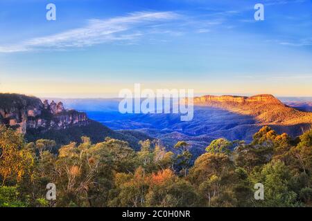 Canyon profond autour de la formation rocheuse de Three Sisters dans les Blue Mountains australiennes, dans une douce lumière du matin au-dessus des sommets des arbres. Banque D'Images