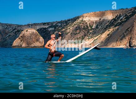 Montez à bord de paddle-board. Un homme fort pratique sur un panneau SUP. L'aventure de la mer avec de l'eau bleue sur un surf. Le concept d'un actif et de guérir Banque D'Images