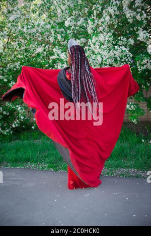 Reine dans la couronne et le manteau royal. Jolie fille sur le fond d'un jardin fleuri. Afro-américain en rouge Banque D'Images