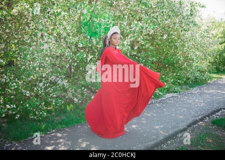 Reine dans la couronne et le manteau royal. Jolie fille sur le fond d'un jardin fleuri. Afro-américain en rouge Banque D'Images