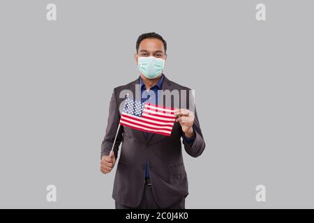 Homme d'affaires portant un drapeau américain portant un masque médical. Homme d'affaires indien debout pleine longueur avec drapeau des États-Unis dans les mains Banque D'Images